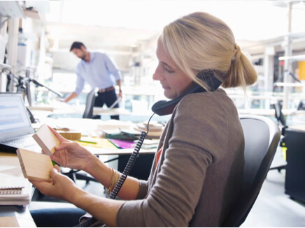 Woman sitting behind files talking on a desk phone.